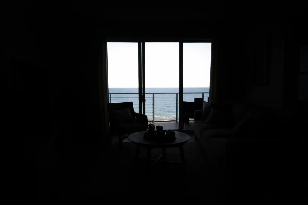 Ein extrem dunkles Wohnzimmer einer Ferienwohnung, fotografiert direkt gegen ein helles Fenster mit Meerblick.